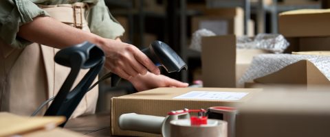 Female seller online store worker holding scanner scanning parcel bar code packing e commerce post shipping box preparing online retail shop order in dropshipping delivery service warehouse.