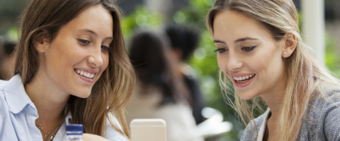 Women looking and pointing at phone while smiling.