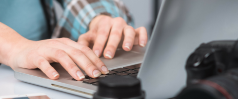 Man working on computer with camera equipment on the desk.